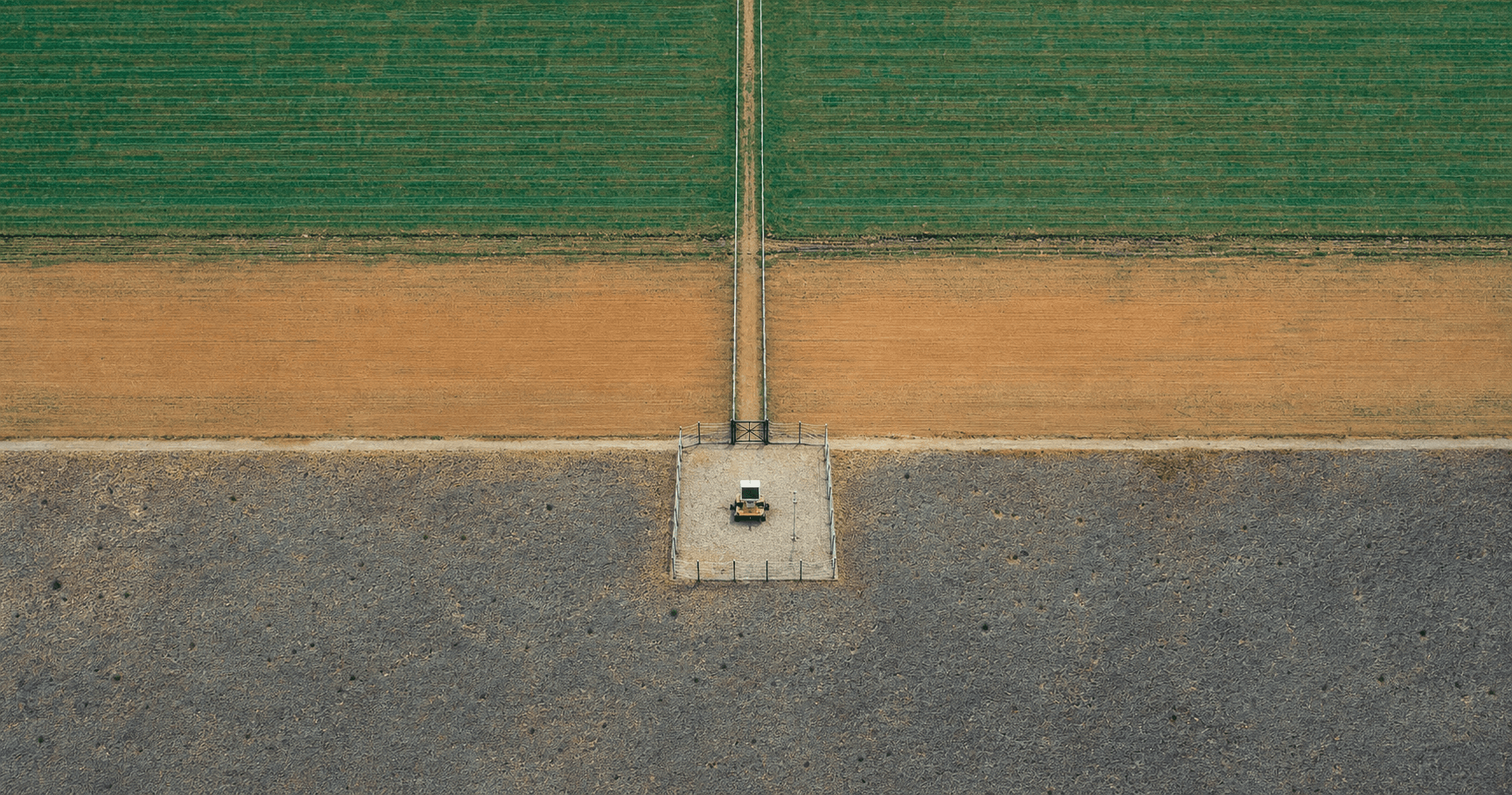 A tiny autonomous machine inside a fenced work zone in an aerial landscape divided into bands